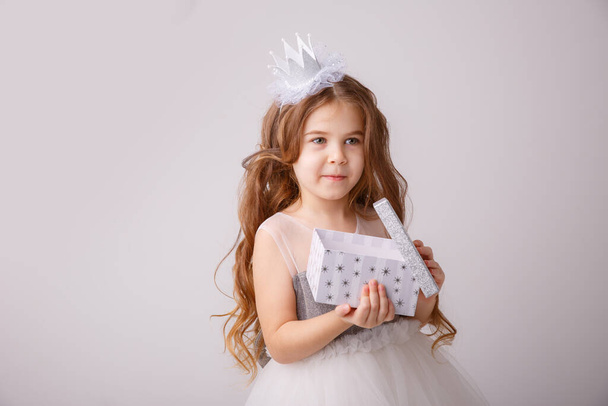 Peri kostümü giymiş küçük bir kız. Elinde bir hediye olan bir prenses. Gri bir arka planda izole edilmiş. - Fotoğraf, Görsel