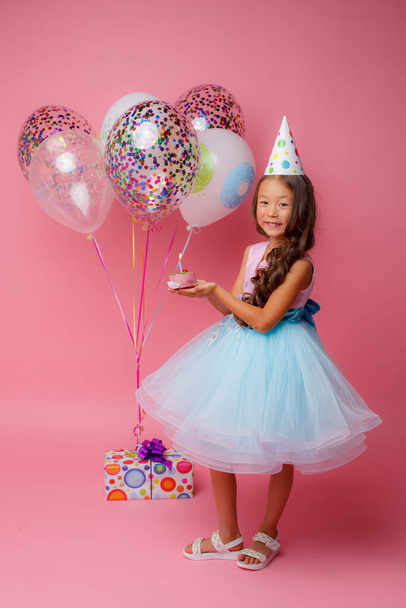 A young Asian girl blows out a candle on a pink background at a birthday party - Photo, Image
