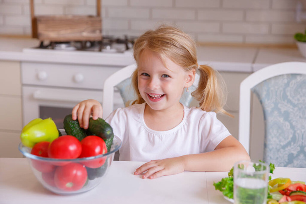 blond baby meisje eten groenten in de keuken - Foto, afbeelding