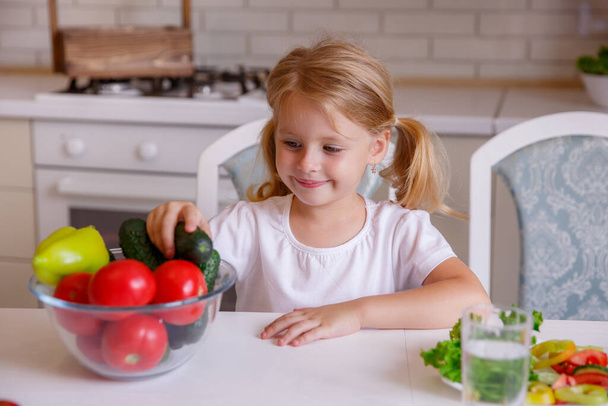 blonde baby girl eating vegetables in the kitchen - Foto, Imagem