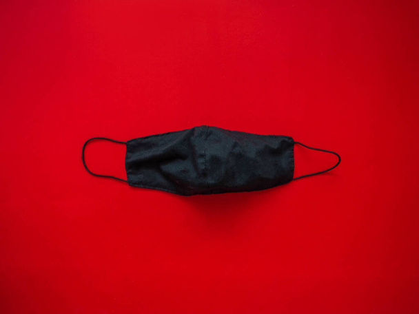 Czarna maska tkaninowa do ochrony przed śliną i kroplami kurzu umieszczonymi na czerwonym tle. Podczas rozprzestrzeniania się wirusa - Zdjęcie, obraz