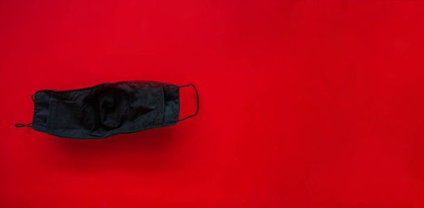 Een zwart doekmasker voor bescherming tegen speeksel en stofdruppels op een rode achtergrond. Tijdens de verspreiding van het virus - Foto, afbeelding