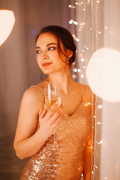 Girl in evening dress posing in the New Year's studio with a glass of champagne - Fotó, kép