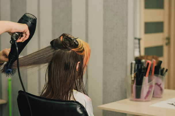Friseur macht eine Frisur zu niedlichen kleinen Mädchen. Ein Teenager-Mädchen lässt sich in einem Schönheitssalon den Pony aufhellen. Orangener Pony. Der Trend zu hellem Haar. - Foto, Bild