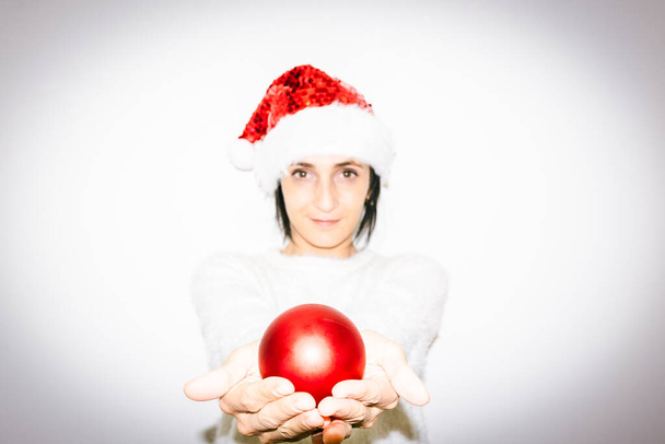 Γυναίκα στα Χριστούγεννα στολή κατέχει σε δύο χέρια κόκκινο Χριστούγεννα διακόσμηση λαμπερό δώρο μπάλα. Ευτυχία και μοιρασιά της αγάπης και της ελπίδας στους εορτασμούς - Φωτογραφία, εικόνα