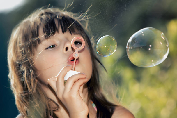 beautiful little girl are blowing soap bubbles on nature outdoor, closeup face - Fotó, kép
