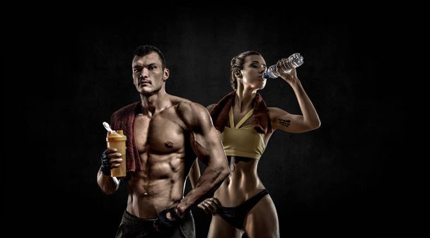 couple man with woman bodybuilders hold shaker with sportive nutrition - protein of shaker on black background with empty space for text. Gym concept - Фото, изображение