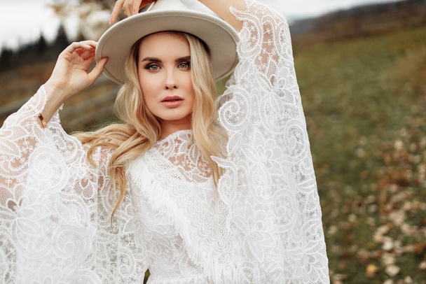 Portrait of adorable woman posing at the field, wearing gorgeous lace dress and white hat, beautiful lady looking at the camera, send out tenderness and charm, women beauty concept - Foto, Imagem