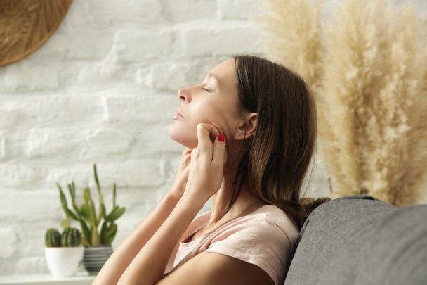 Молода жінка робить анти-старіння масаж обличчя вдома. Концепція домашнього спа та догляду за шкірою
.  - Фото, зображення