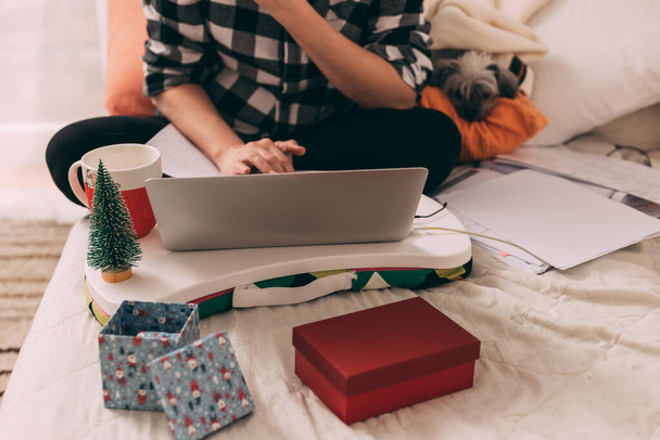 Woman typing on laptop in Christmas ambient with little dog next to her - Photo, Image