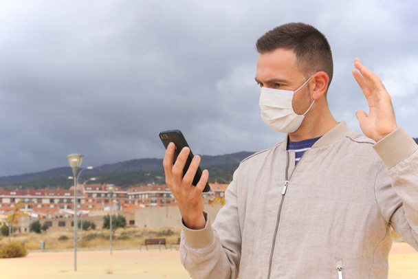 Ο άνθρωπος που φοράει επαναχρησιμοποιήσιμη μάσκα προσώπου χρησιμοποιεί ένα smartphone σε αστικό φόντο. Επαναχρησιμοποιήσιμες μάσκες είναι μια οικολογική εναλλακτική λύση για αναπνευστήρες μιας χρήσης, όπως KN95, FFP2, ή χειρουργικές μάσκες. - Φωτογραφία, εικόνα