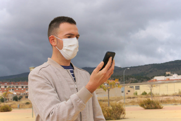 Az újrahasználható arcmaszkot viselő férfi okostelefont használ városi környezetben. Az újrahasználható maszkok ökológiai alternatívái az egyszer használatos légzőkészülékeknek, mint például a KN95, FFP2 vagy sebészeti maszkok. - Fotó, kép