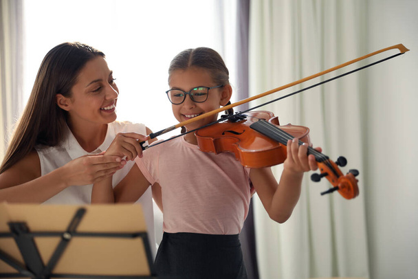 Young woman teaching little girl to play violin indoors - Foto, imagen
