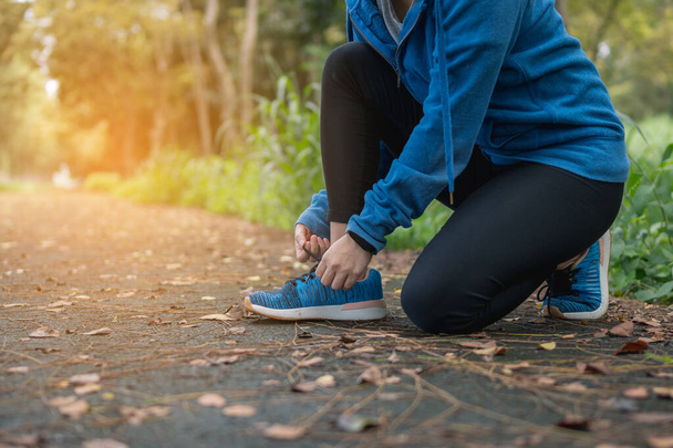 Koşucu koşmadan önce ormanda ayakkabı bağlıyor. Spor ayakkabılarını dışarıda giyen bir kadın..   - Fotoğraf, Görsel