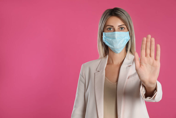 Woman in protective mask showing stop gesture on pink background, space for text. Prevent spreading of coronavirus - Foto, Imagen