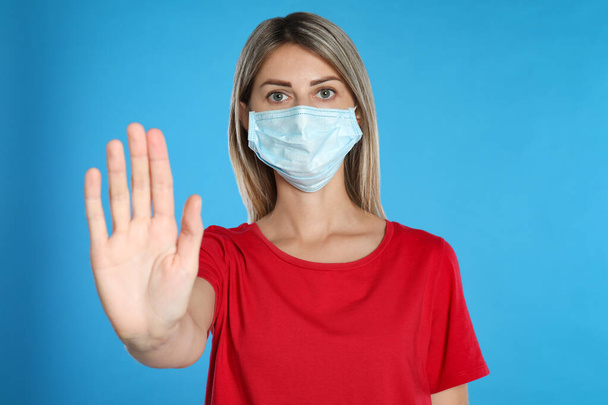 Woman in protective mask showing stop gesture on light blue background. Prevent spreading of coronavirus - Fotoğraf, Görsel