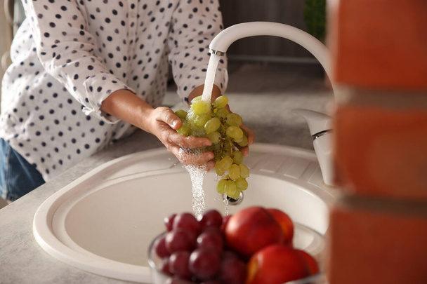 Woman washing fresh grapes in kitchen sink, closeup - Photo, image