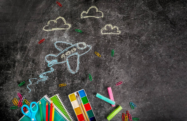 Σχολικές προμήθειες και αεροπλάνα ζωγραφισμένα με κιμωλία σε φόντο μαυροπίνακα. Επιστροφή στο σχολείο έννοια. - Φωτογραφία, εικόνα