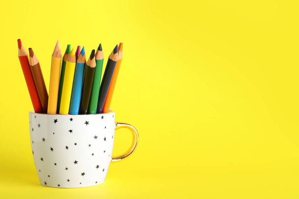 Colorful pencils in cup on yellow background. Space for text - Valokuva, kuva