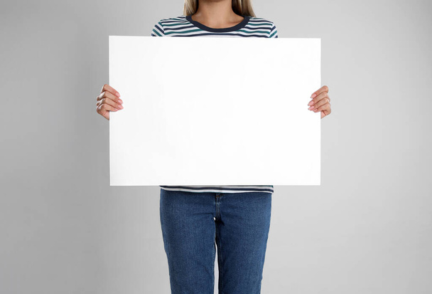 Woman holding blank poster on light grey background, closeup - Zdjęcie, obraz