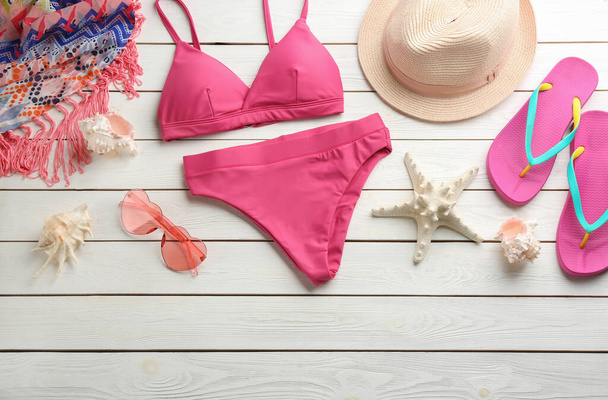Beautiful pink bikini and beach accessories on white wooden background, flat lay - Foto, Imagen