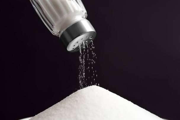 Pouring salt from shaker on black background, closeup - Photo, image