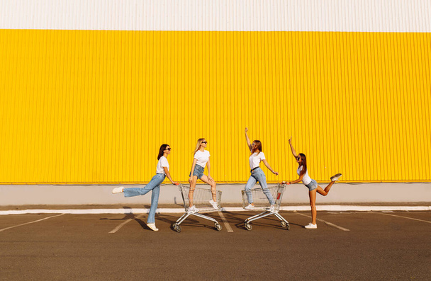 Skupinové mladé přátele, mladé ženy baví, jízda na kočárech v létě slunečný den v blízkosti nákupního centra - Fotografie, Obrázek