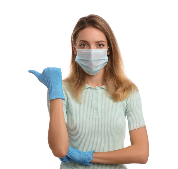 Young woman in medical gloves and protective mask pointing thumb aside on white background - Фото, изображение