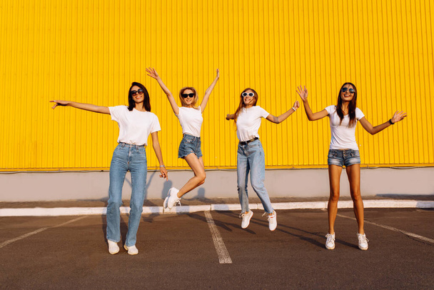 Excited group of friends having fun and jumping against yellow wall background on sunny summer day - Foto, Imagen