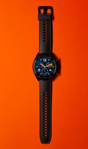Крупный план черных умных часов на оранжевом фоне, похожих на часы лица. Технология и элегантность концепции. Вертикальная фотография. Копирование пространства - Фото, изображение