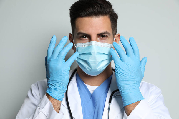 Médico en máscara protectora y guantes médicos contra fondo gris claro - Foto, Imagen