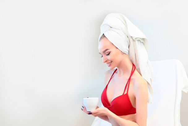 The woman tied a white terry towel around her head. Wellness concept. Spa. Copy space. Photo on a white background. A white cup with tea in a woman's hand. - Zdjęcie, obraz