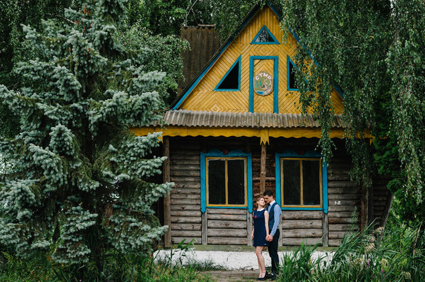 A young couple standing and hugging near a wooden old house on an island in the forest between trees. House on the background of trees. Nature, landscape. - Valokuva, kuva