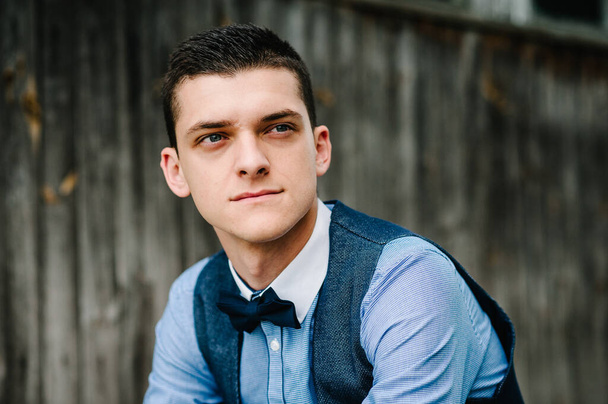 Portrait young beautiful man sitting next to the wooden wall of an old house. looking sideways. upper half length. businessman. Close up. headshot. - 写真・画像