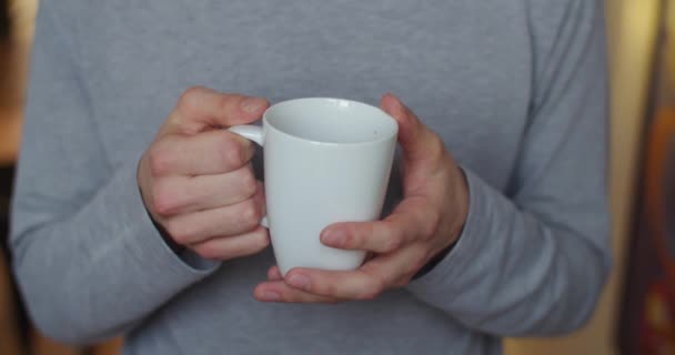 Передній вигляд чоловічих рук, що тримають білу чашку в приміщенні повільний рух крупним планом. Безликий чоловік п'є чай, освічений ранковим природним світлом. Енергія сніданку здоровий спосіб життя. звички охорони здоров'я
 - Кадри, відео