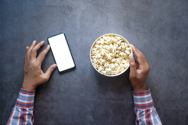 ręka człowieka za pomocą smartfona i jedzenia popcornu  - Zdjęcie, obraz