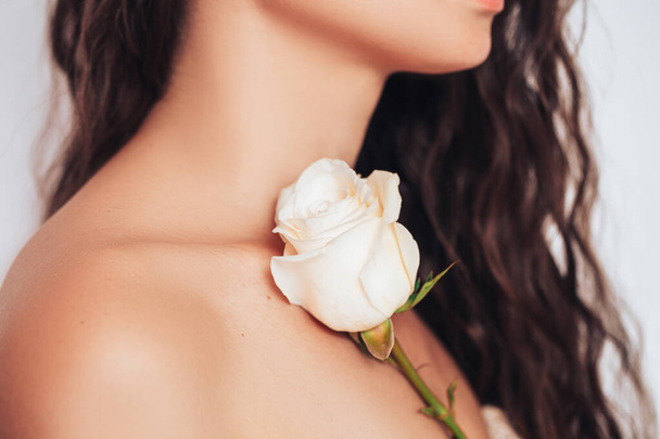 Nuori nainen valkoisella taustalla löysät hiukset laittaa vaaleanpunainen ruusu olkapäällään. - Valokuva, kuva