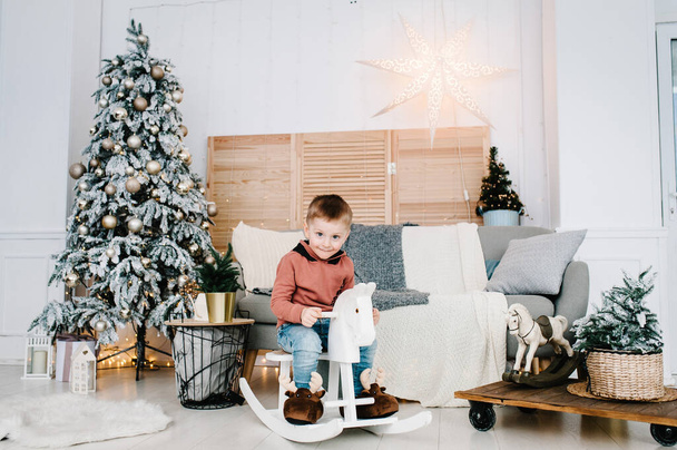 Boy playing near Christmas tree. Happy New Year and Merry Christmas. Christmas decorated interior. The concept of family holiday. - Valokuva, kuva