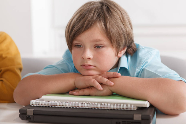 Üzgün görünen, okul kitaplarının ve dizüstü bilgisayarlarının üzerinde dinlenen küçük şirin bir çocuğun yakın çekimi. - Fotoğraf, Görsel