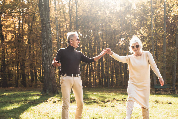 Senior man flirting and dancing with elderly grey haired woman. Happy elderly people enjoying sunny autumn day in park.  - Фото, изображение