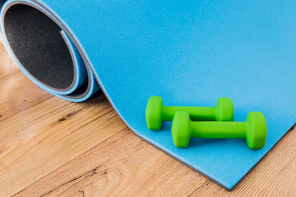Dois halteres verdes jazem no tapete de fitness. Conceito de esportes, fitness, exercícios em casa. - Foto, Imagem