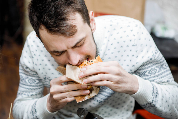 El joven está comiendo una hamburguesa en una mesa en un café. - Foto, imagen