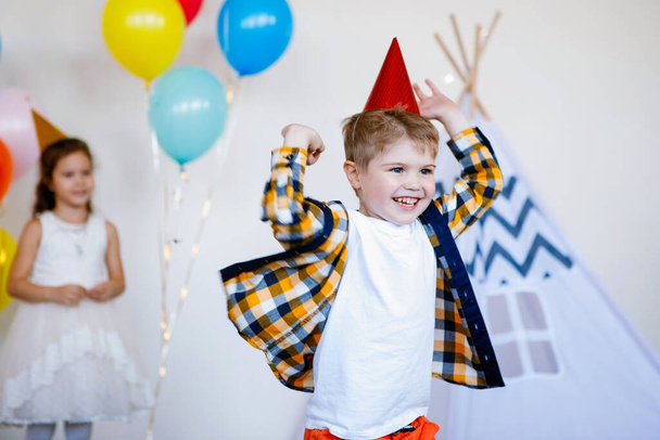 誕生日のお祝いに帽子をかぶった男の子を笑っています。多色気球の背景. - 写真・画像