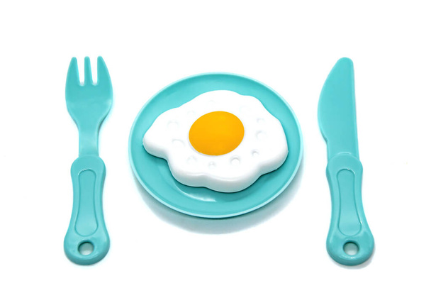 Children's toy plastic tableware: plate with fried eggs, fork and knife. Serving set. Developing role-playing games for children. Kitchen utensils, household training. Kid's Kitchen. - Photo, Image