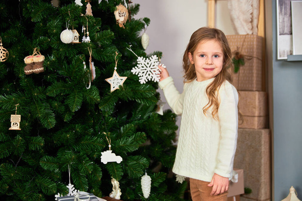 A little cute girl holds a toy for a Christmas tree in her hands. - 写真・画像