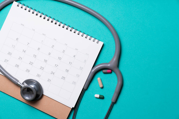 Top view of stethoscope, drug and calendar on the green background, schedule to check up healthy concept - Photo, image