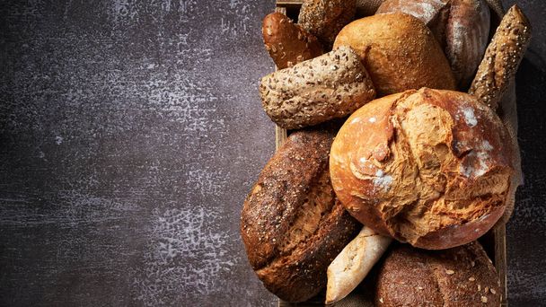 Banner with Different Types of Bread put in a wooden box on dark background. Close up. Bakery concept. Empty space for text. - Photo, Image