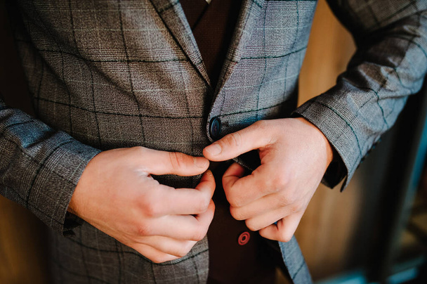 Man fastens the buttons jacket. The groom in a suit, shirt is standing on room background. Close up. - Fotó, kép