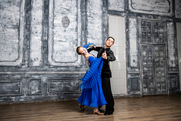 молодий чоловік танцює з дівчиною в блакитній бальній сукні в сірому танцювальному залі
 - Фото, зображення