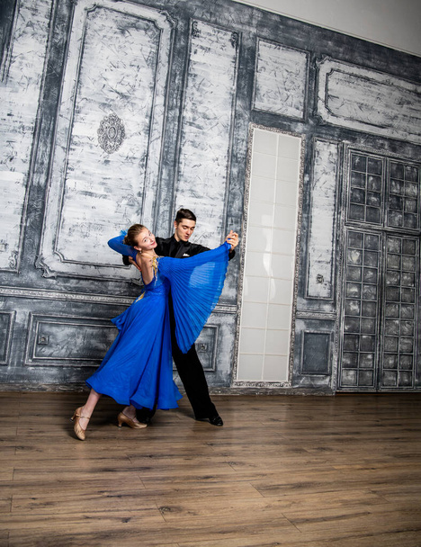 mladý muž tančí s dívkou v modrých tanečních šatech v šedém tanečním sále - Fotografie, Obrázek